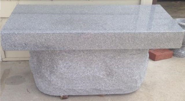 A gray granite bench is sitting on a concrete floor.