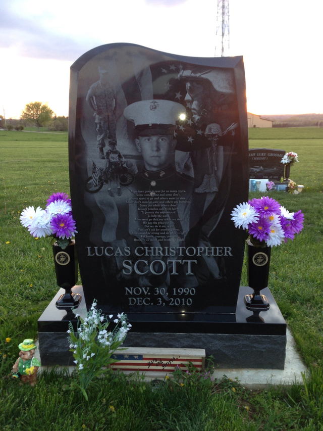 A gravestone for lucas christopher scott in a cemetery with purple and white flowers.