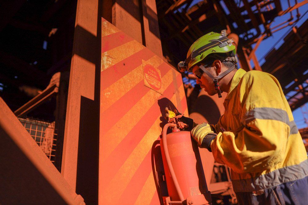 Worker in Yellow Safety Gear Checks a Red Fire Extinguisher — Hunter Fire & Safety in Edgeworth, NSW