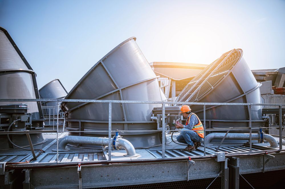 Man in Hard Hat and Vest Inspecting Cooling Towers on a Rooftop — Hunter Fire & Safety in Lake Macquarie, NSW