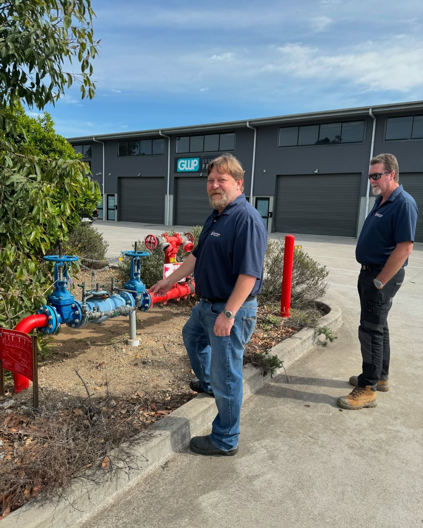 Two Men Near Blue and Red Water Pipes Outside a Commercial Building — Hunter Fire & Safety in Edgeworth, NSW