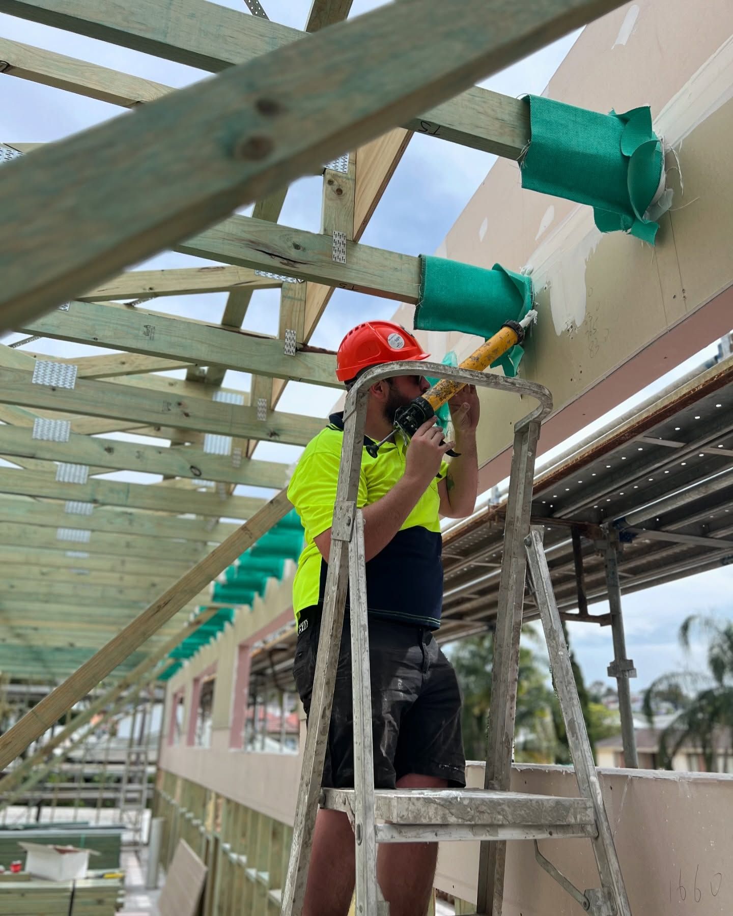 Construction Worker on a Ladder, Caulking Green Ductwork — Hunter Fire & Safety in Edgeworth, NSW