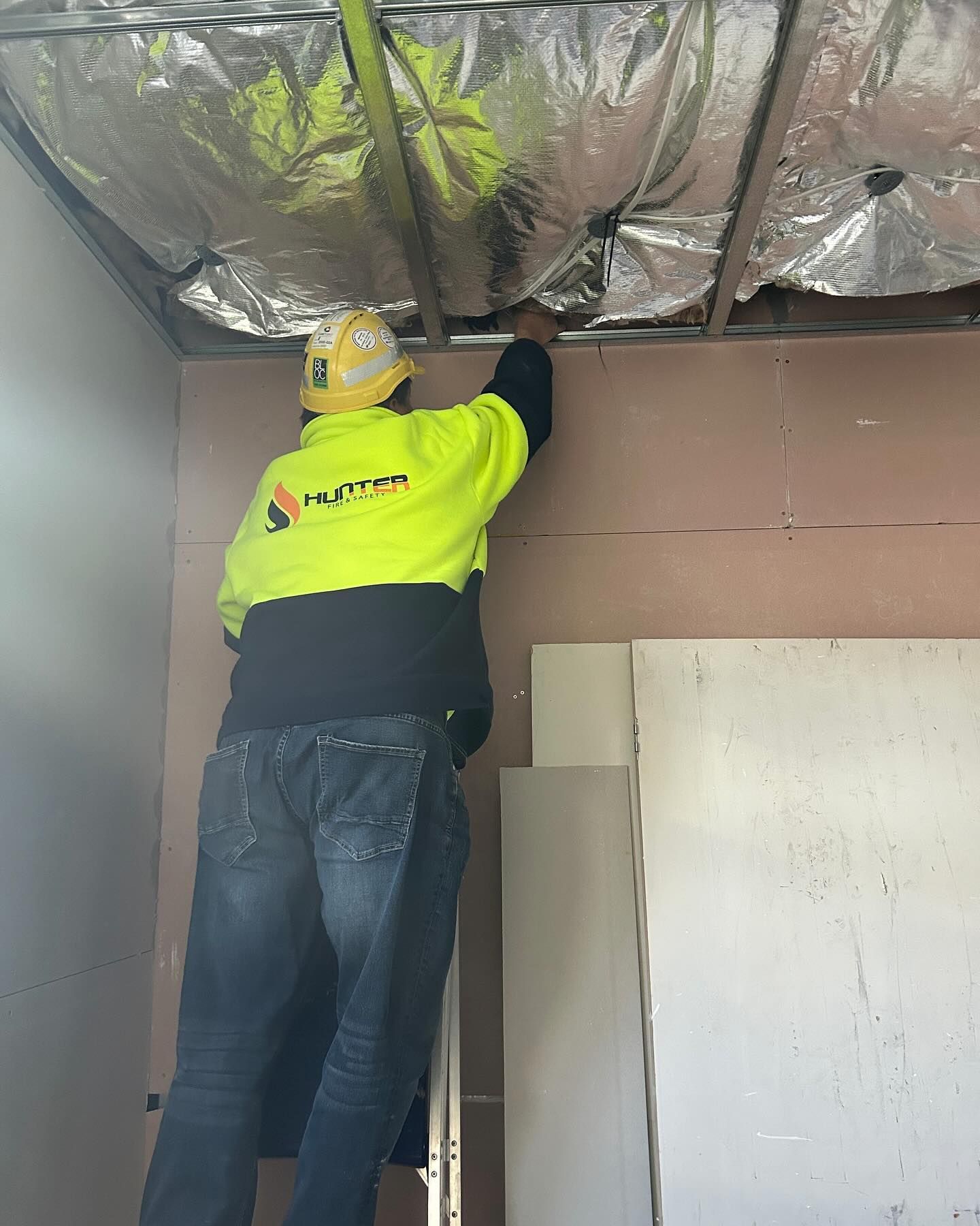 Construction Worker Installing Wallboard on a Ladder, Reflective Insulation Above — Hunter Fire & Safety in Edgeworth, NSW