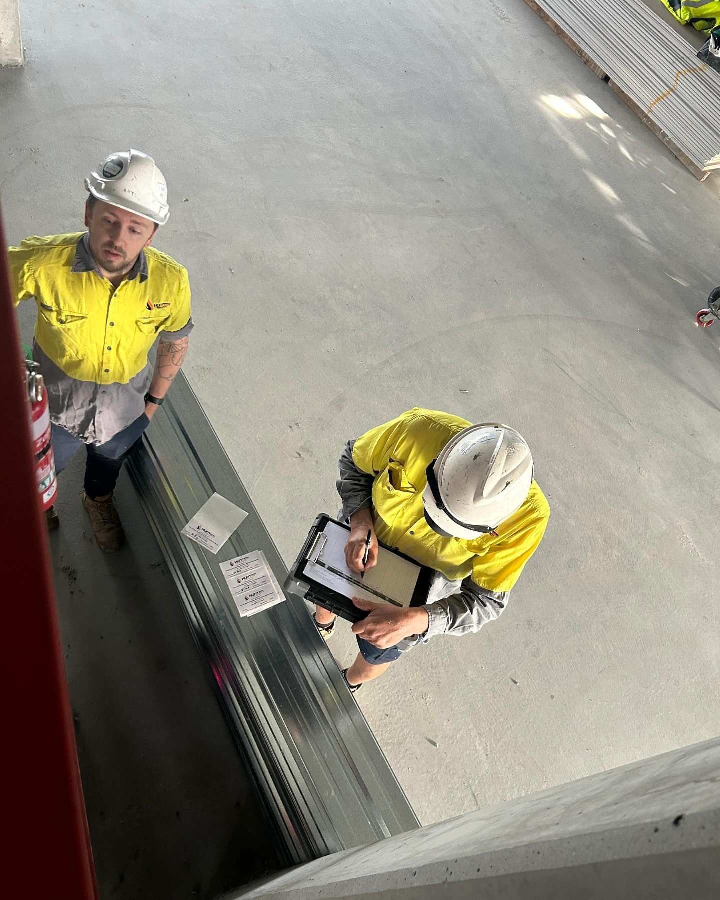 Two Construction Workers in Yellow Shirts and Hard Hats Inspecting a Building Site — Hunter Fire & Safety in Edgeworth, NSW