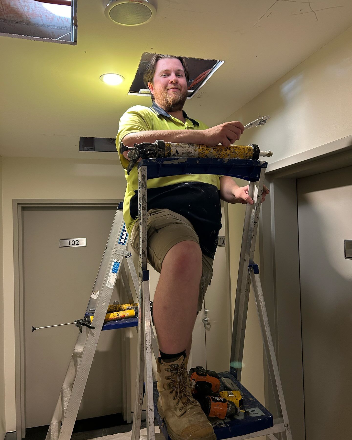 Man on a Ladder Working on Ceiling Fixture, Wearing Work Clothes — Hunter Fire & Safety in Edgeworth, NSW