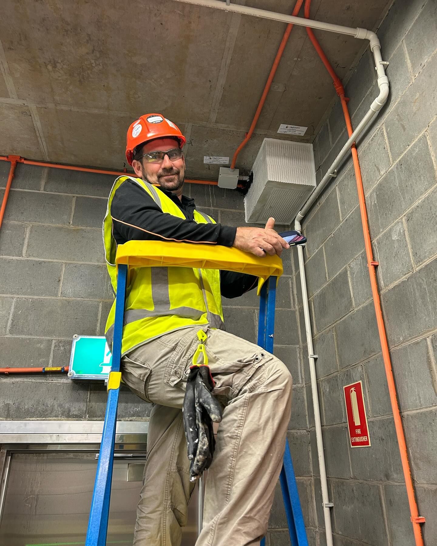 Man on a Ladder in a Building, Wearing a Hard Hat and Safety Vest, Working on Wiring — Hunter Fire & Safety in Edgeworth, NSW