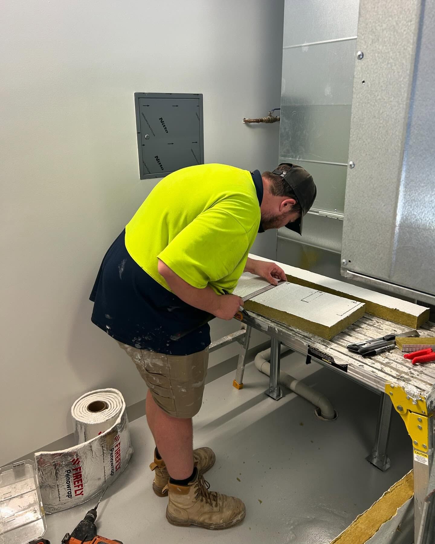 Construction Worker in Safety Vest Measures and Cuts Insulation — Hunter Fire & Safety in Edgeworth, NSW
