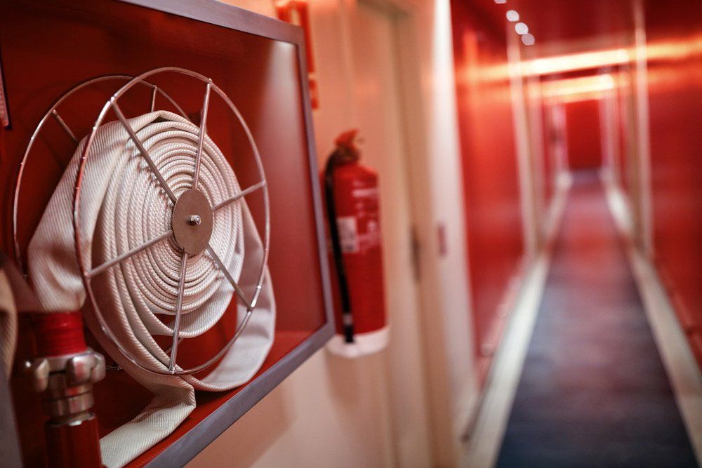 Fire Hose Reel in a Red-walled Hallway With Fire Extinguisher — Hunter Fire & Safety in Edgeworth, NSW