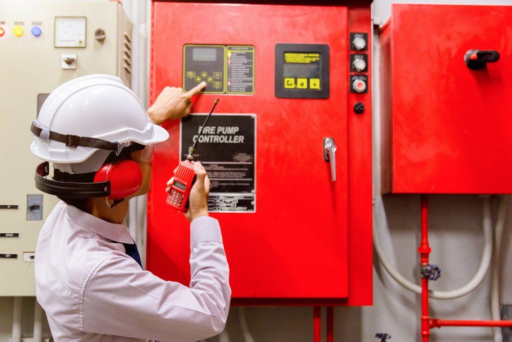 Person in a Hard Hat and Earmuffs Points at Fire Pump Controller in a Red Panel — Hunter Fire & Safety in Port Stephens, NSW
