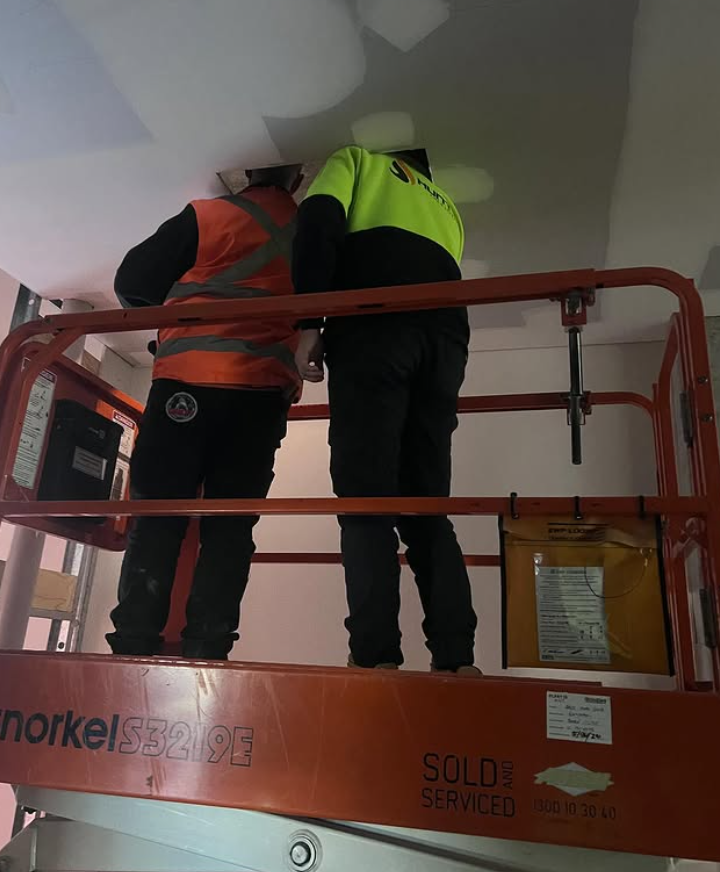 Two Workers on an Orange Lift Platform Install Something in a Ceiling — Hunter Fire & Safety in Edgeworth, NSW