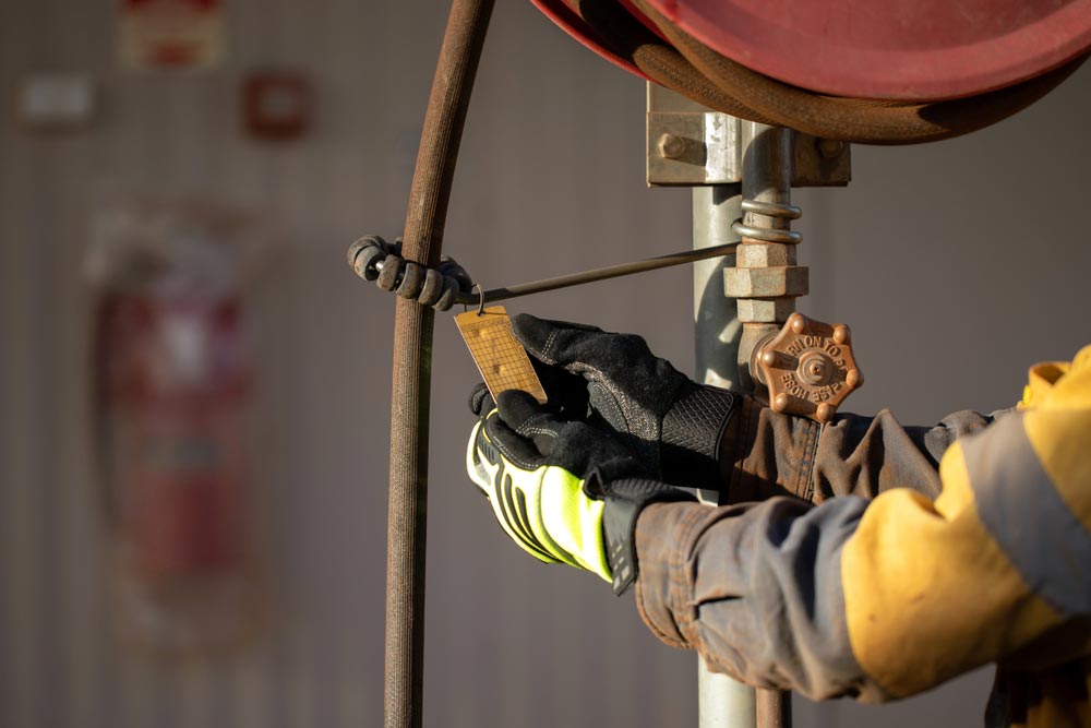 A Person in Work Gloves Attaching a Tag to a Pipe Valve Outside a Building — Hunter Fire & Safety in Port Stephens, NSW