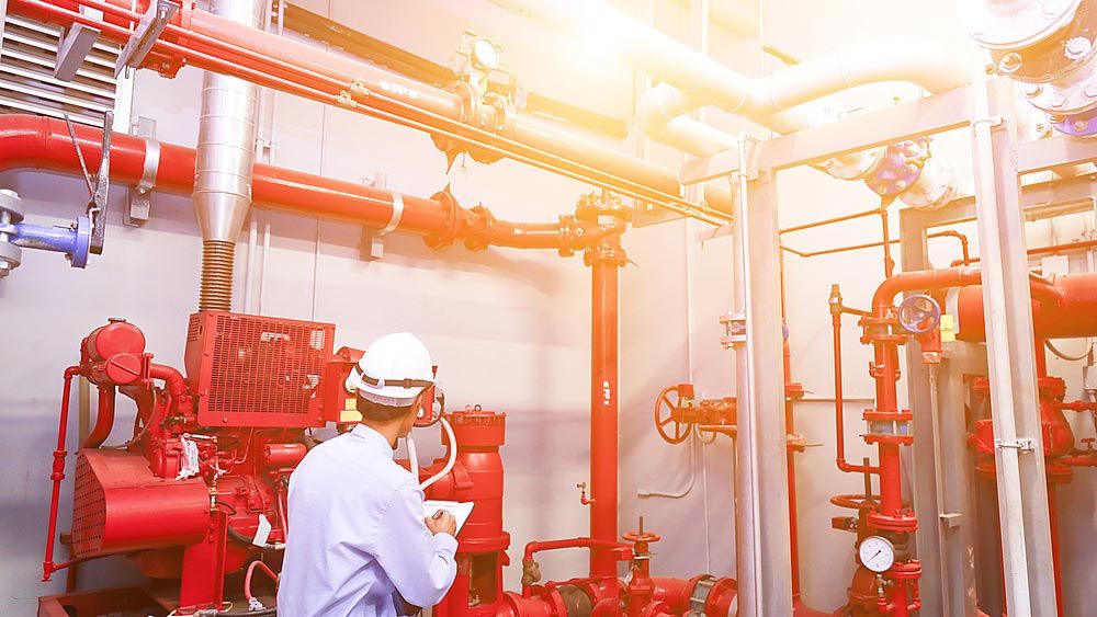 Engineer in a Hard Hat Inspecting Red Pipes and Equipment in a Machinery Room — Hunter Fire & Safety in Edgeworth, NSW
