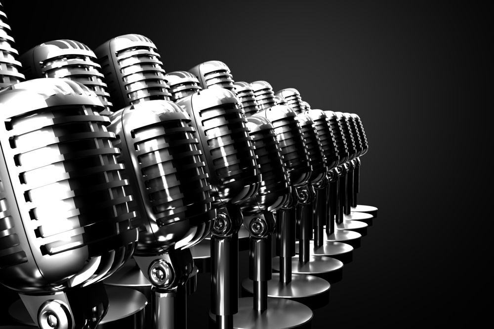 A row of microphones are lined up in a row on a black background.