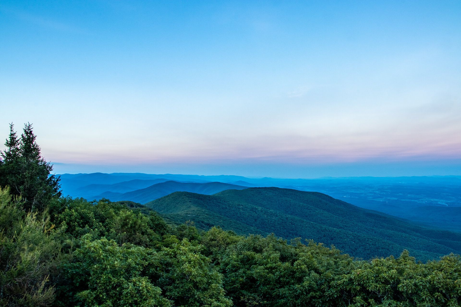 Mountains covered in green trees under a gradient blue sky at dusk.