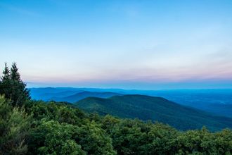 Mountains covered in green trees under a gradient blue sky at dusk.