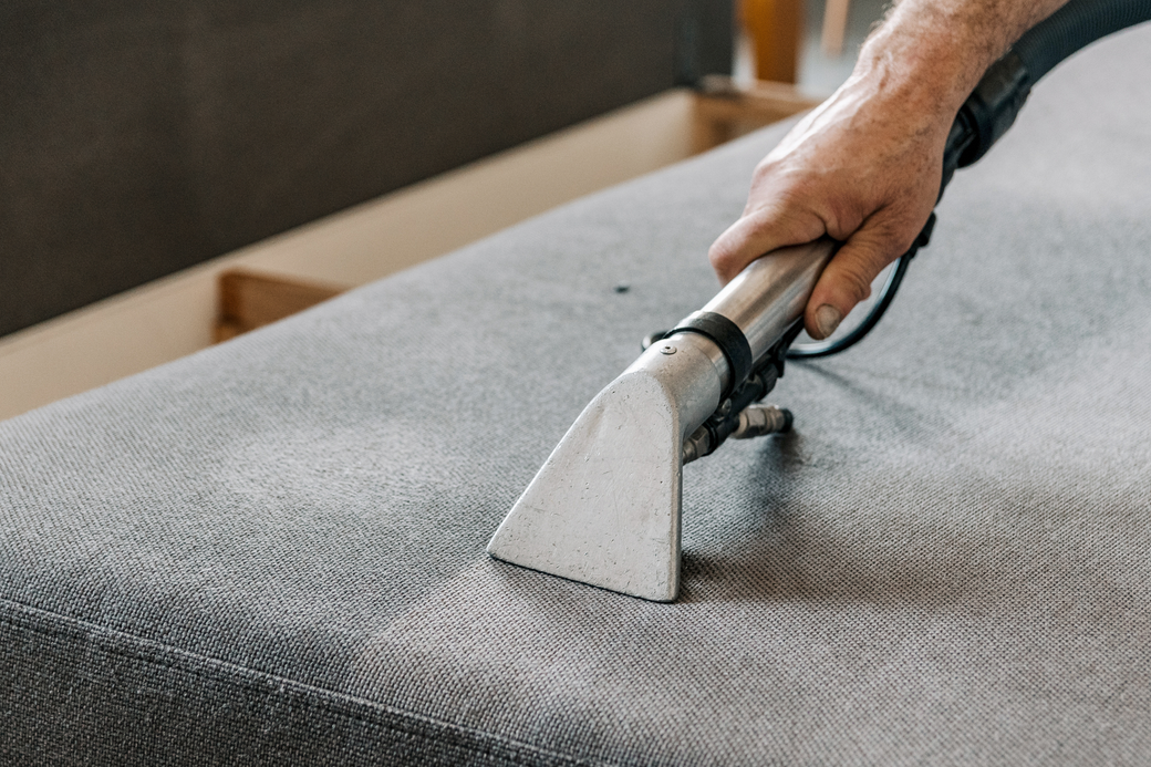 A person is cleaning a couch with a vacuum cleaner.