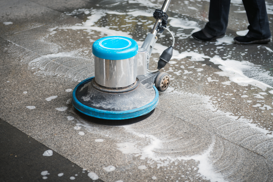 A person is cleaning a tiled floor with a machine.