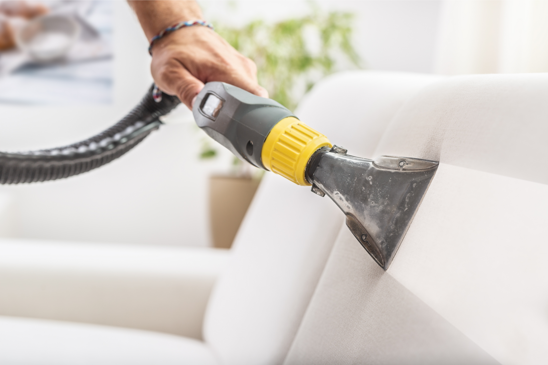 A person is cleaning a couch with a vacuum cleaner.