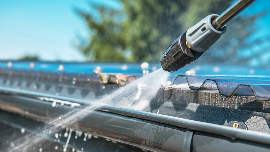 A person is using a high pressure washer to clean a gutter.