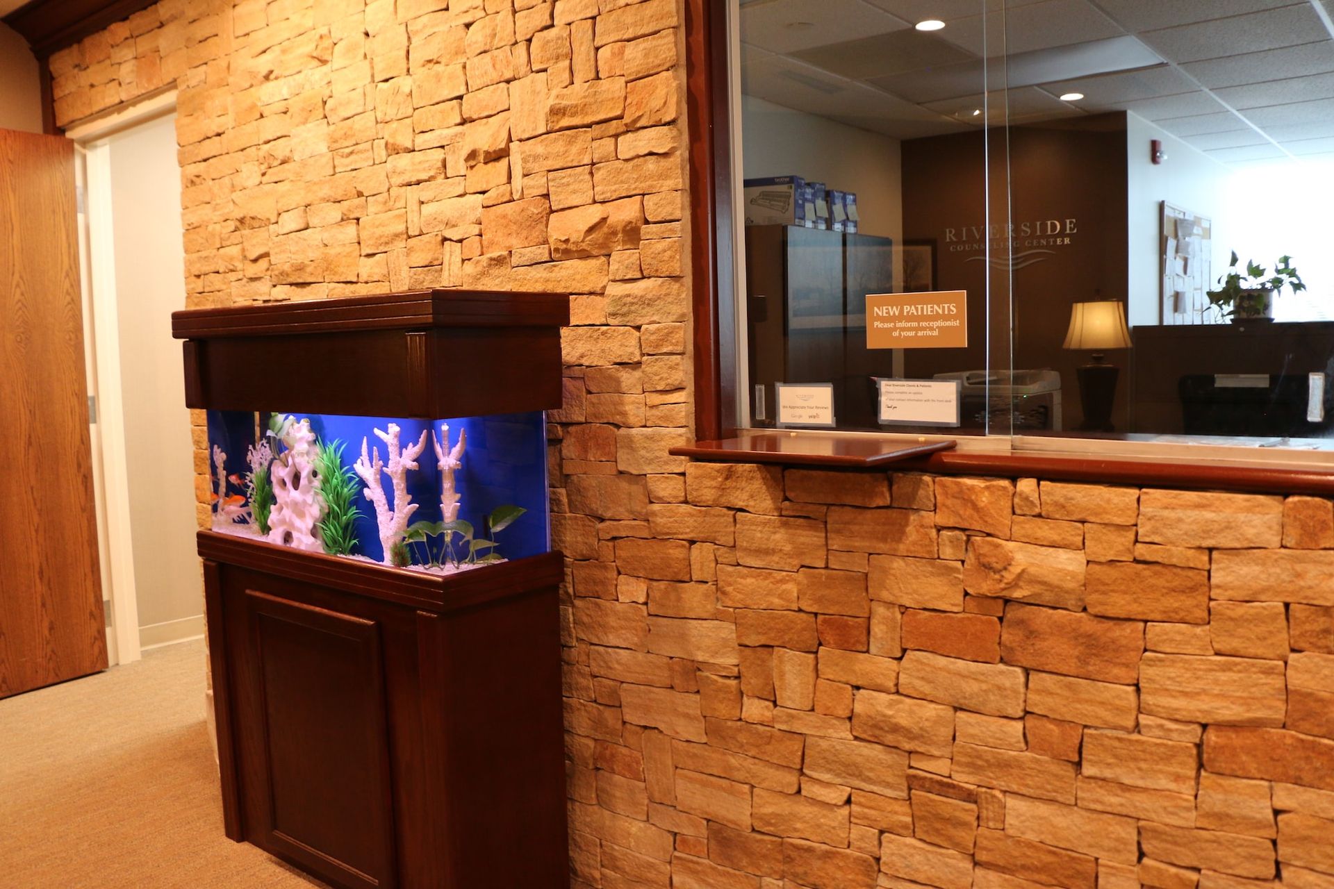 A large aquarium is sitting in a hallway next to a brick wall.