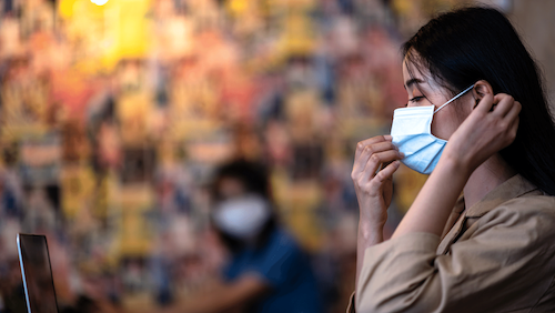 A woman wearing a face mask is sitting in front of a laptop computer.