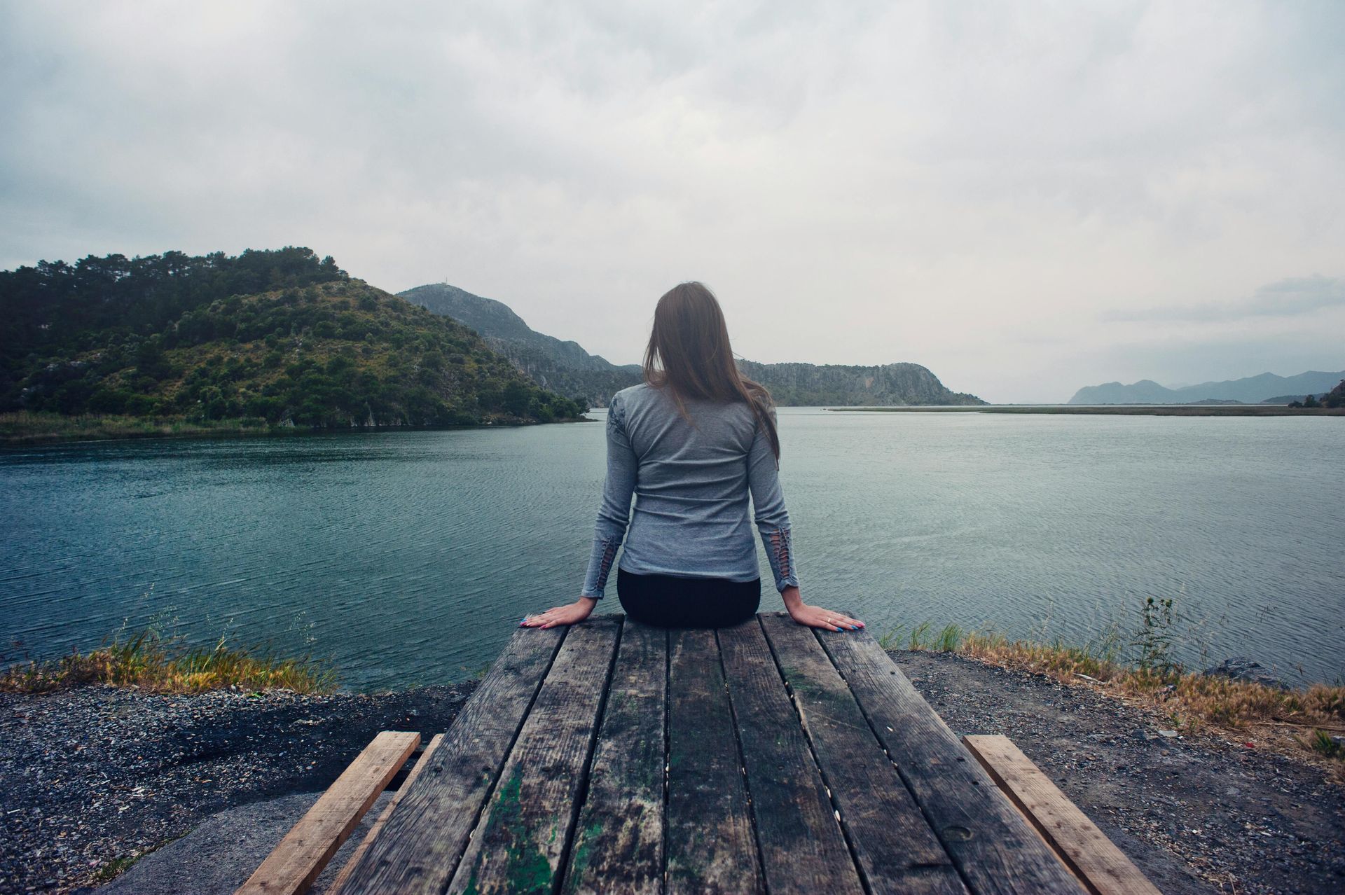 A woman is sitting on a wooden dock overlooking a lake.