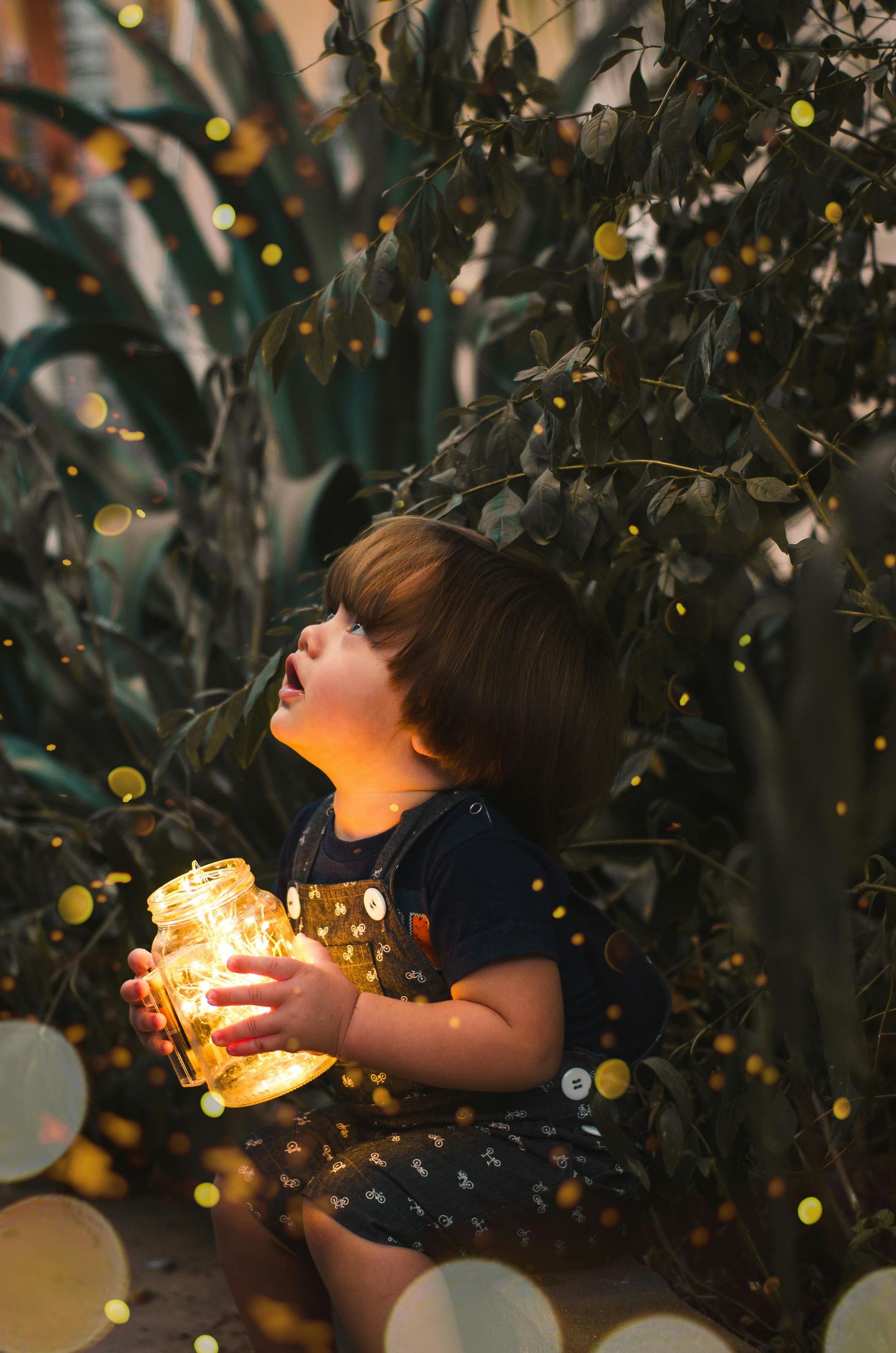 A little girl is sitting under a tree holding a light.