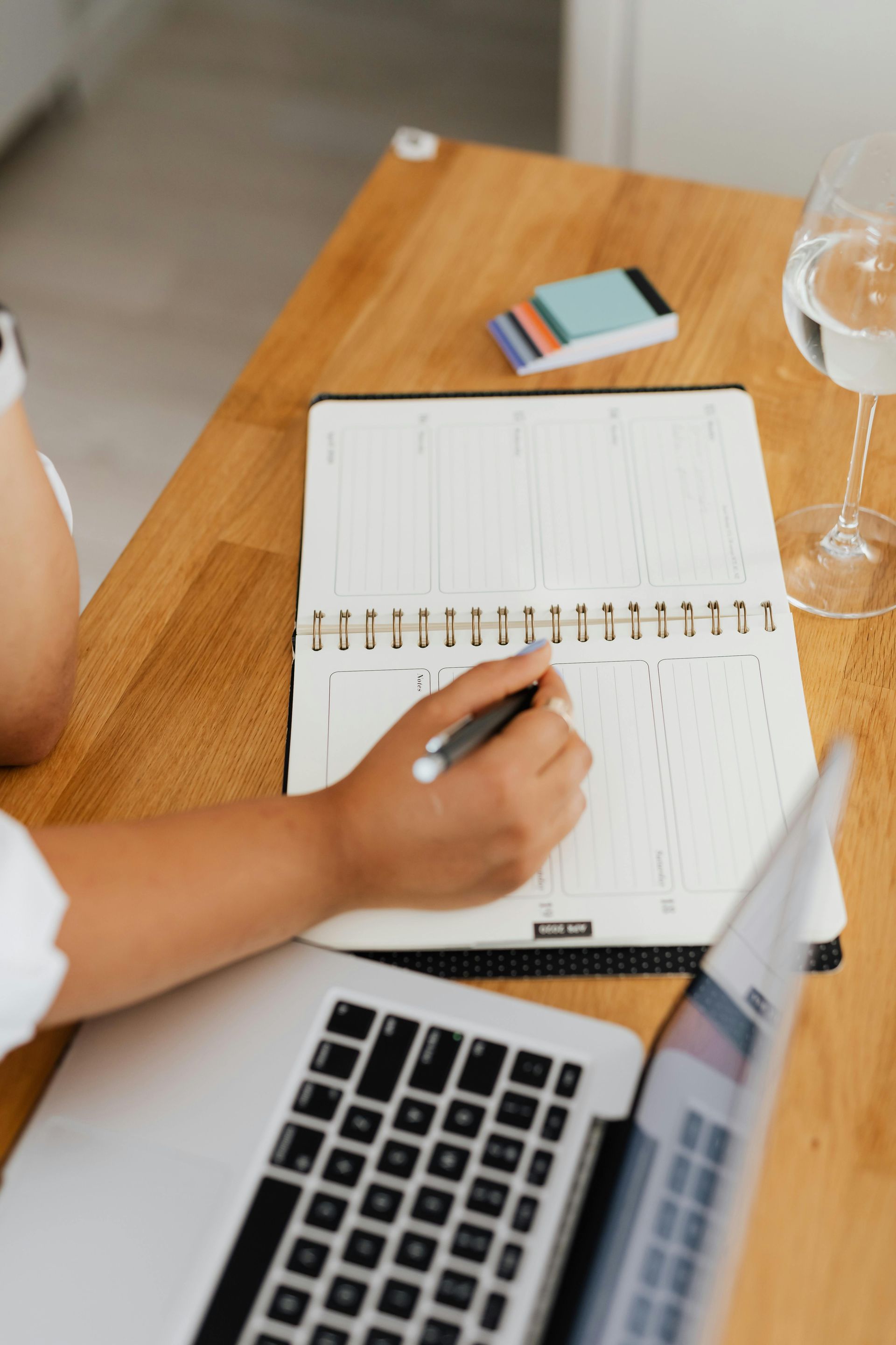 A person is writing her appointment for therapy in a notebook next to a laptop.