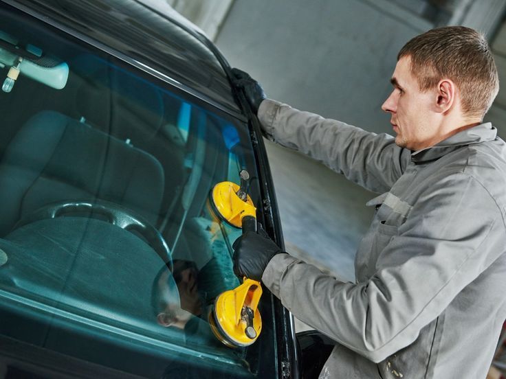 Man using yellow suction tools to repair a car windshield in a garage