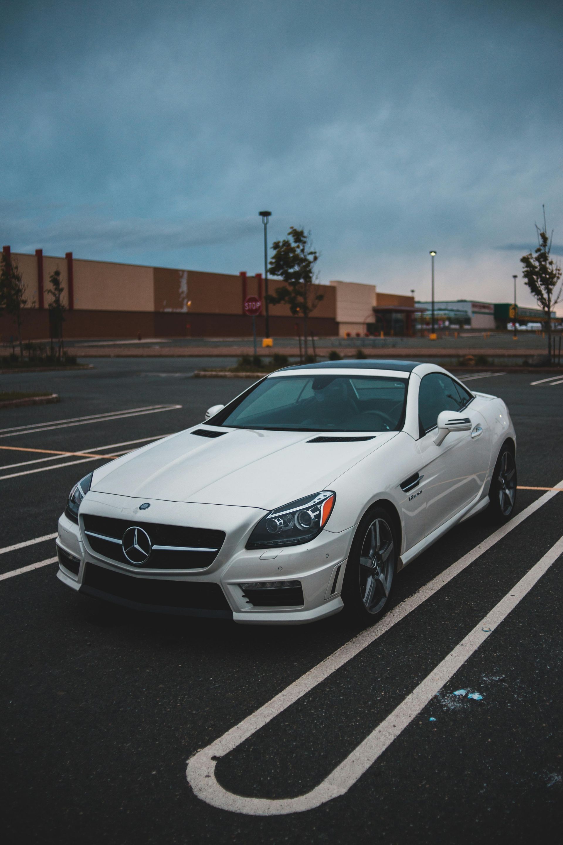 A sleek white convertible car parked in an empty lot under a cloudy sky.