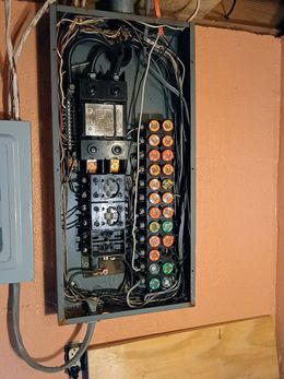 A very messy electrical box is hanging on a wall.