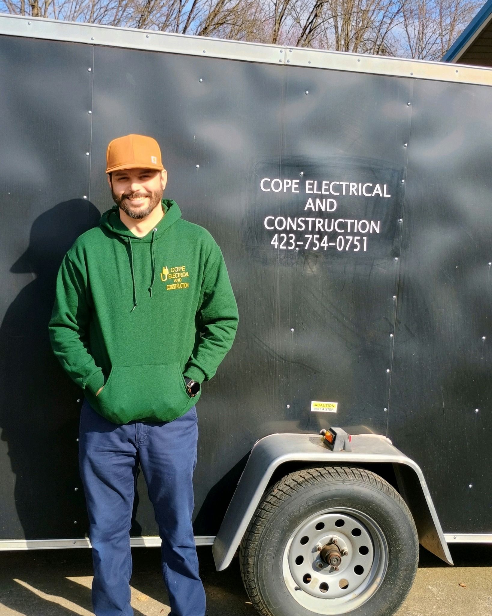 A man is standing in front of a trailer that says copper electrical and construction