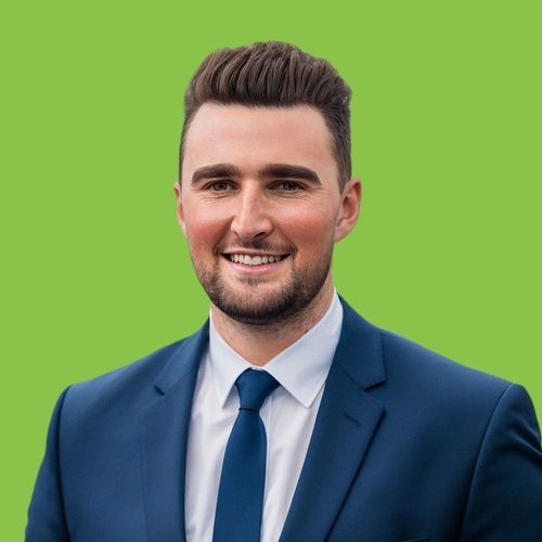 A man in a suit and tie is smiling in front of a green background.