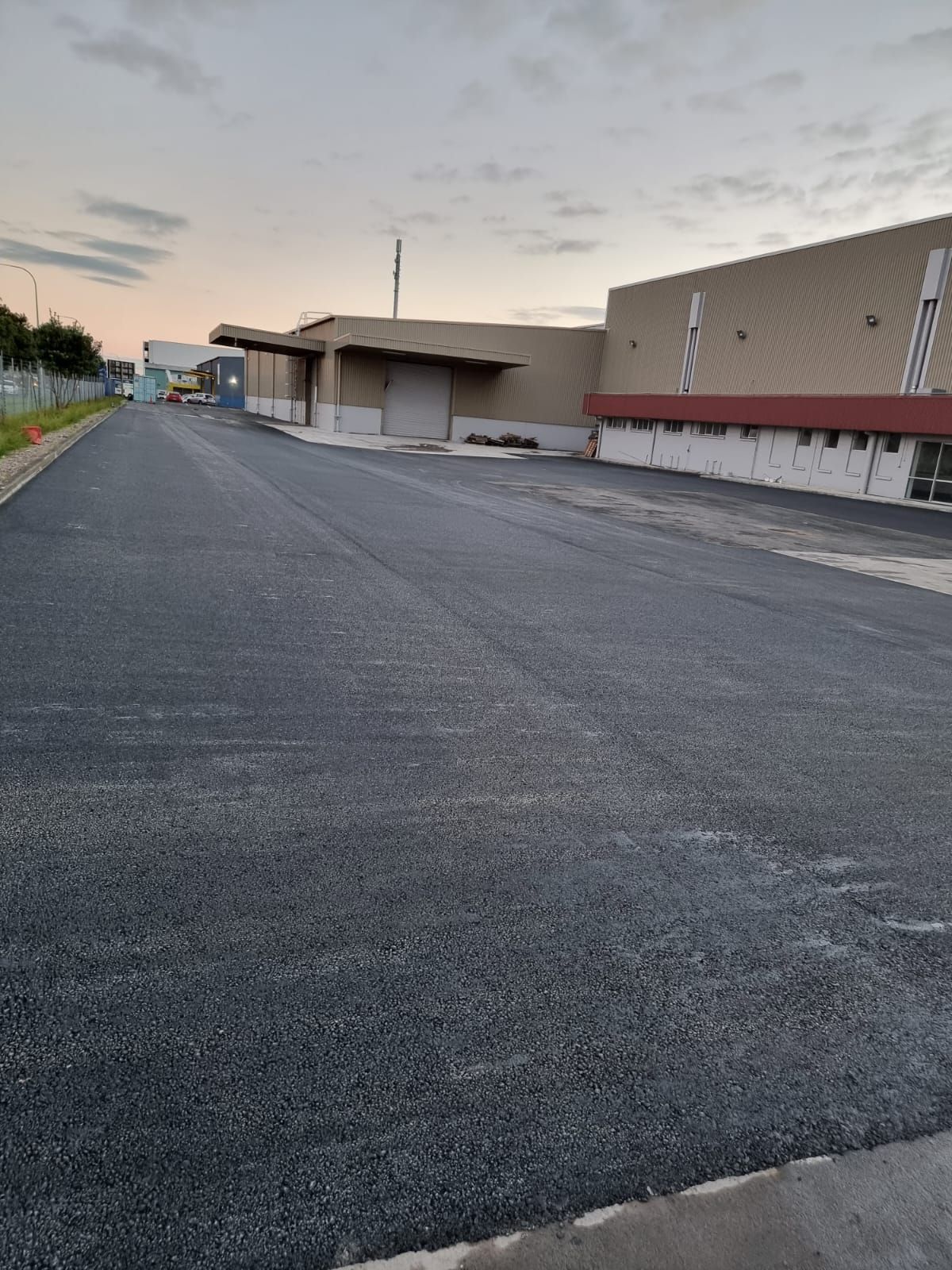 A road with a building in the background and a lot of gravel on the side of it.