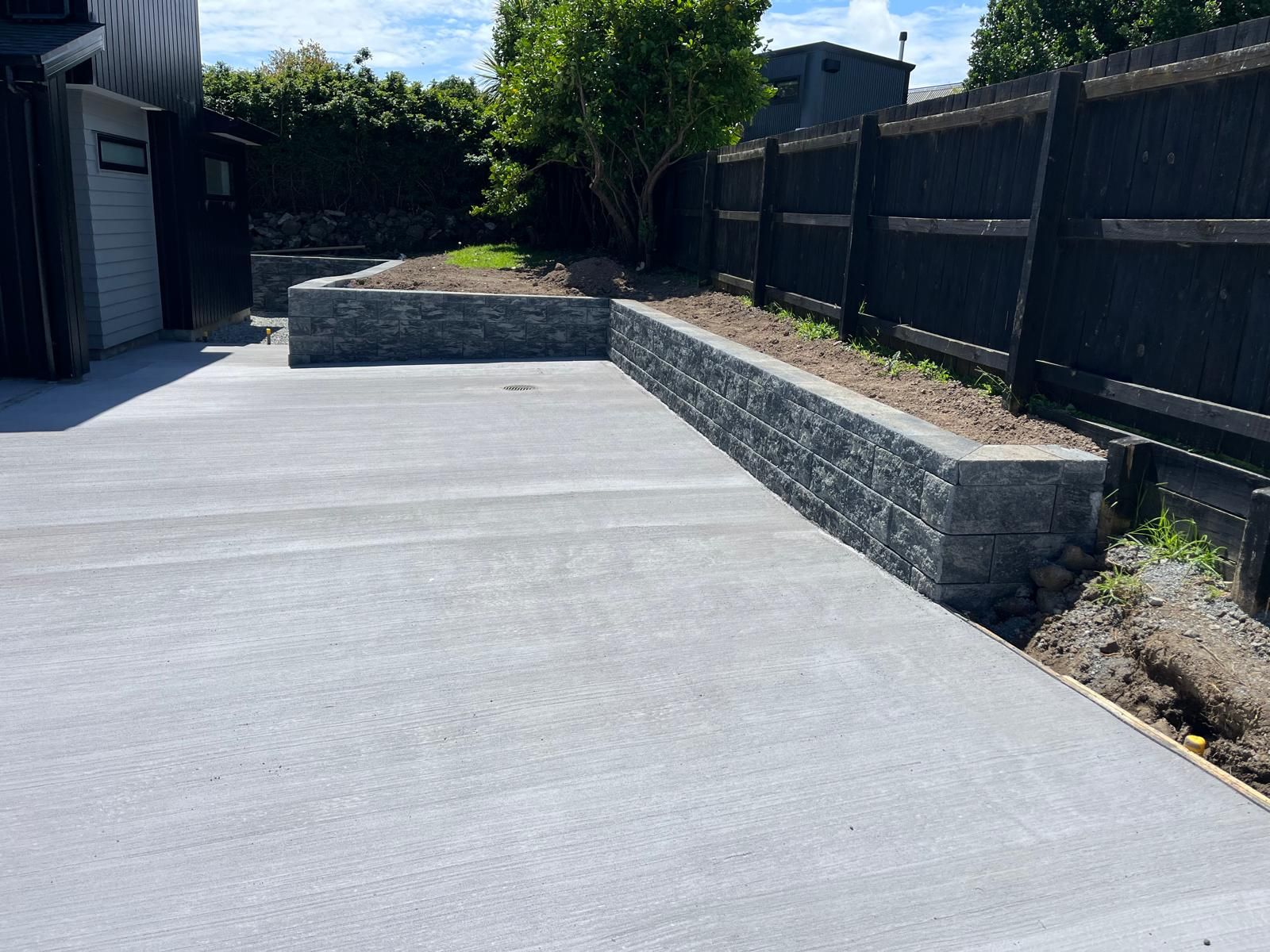 A concrete driveway with a stone wall and a fence in the background.
