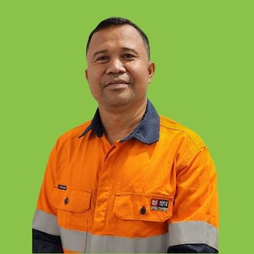 A man in an orange safety vest is standing in front of a green background.