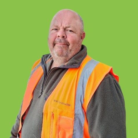 A man wearing an orange vest is standing in front of a green background.