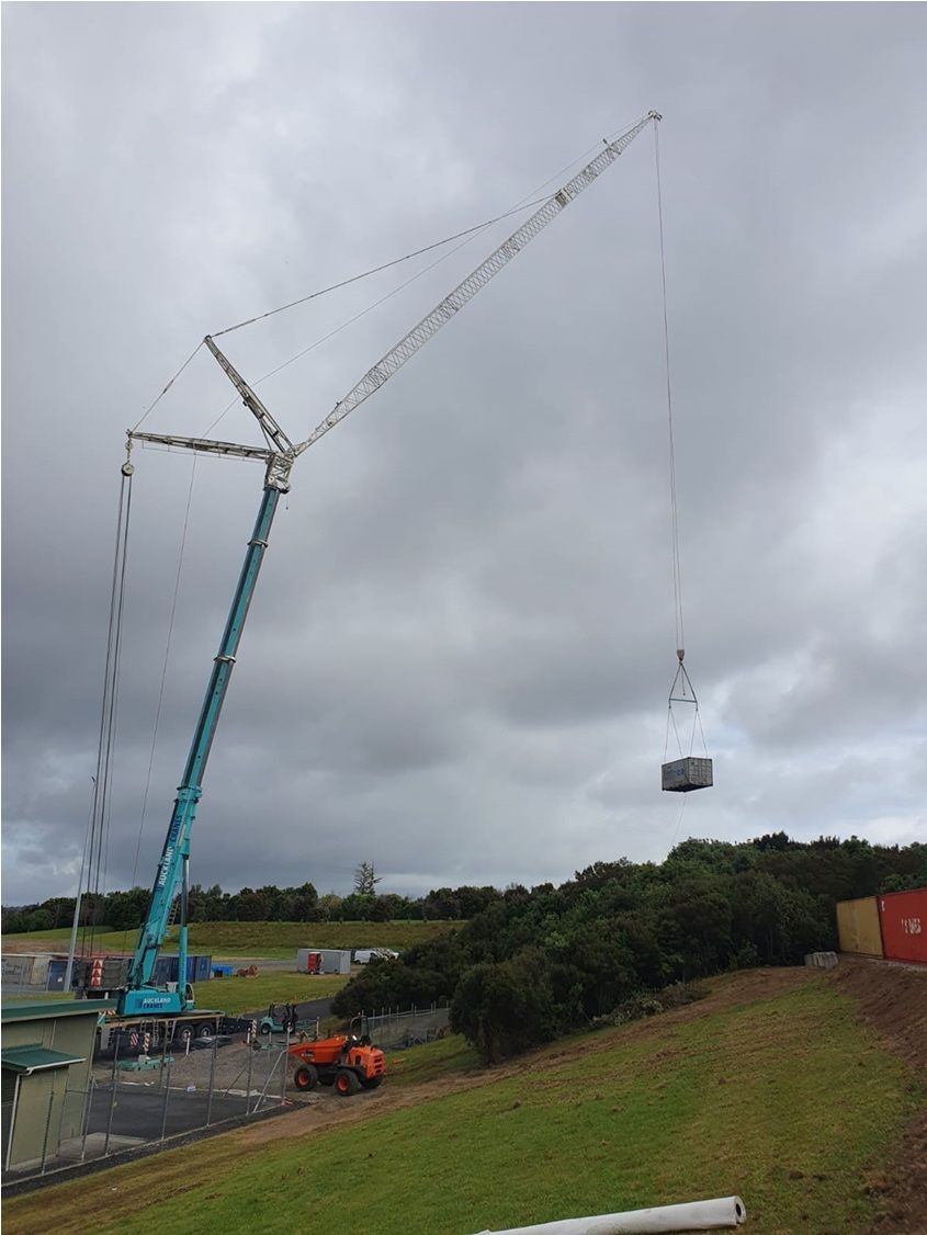 A large crane is lifting a container in a field.
