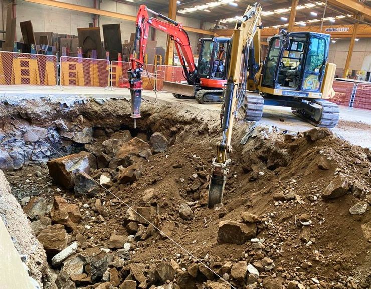 A large excavator is digging a hole in the dirt in a warehouse.