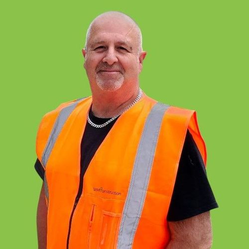 A man wearing an orange vest is standing in front of a green background.