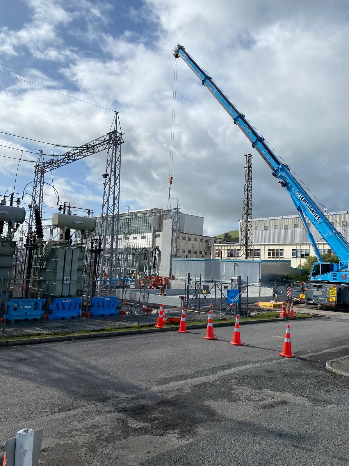 A blue crane is being used to lift a transformer at a construction site.