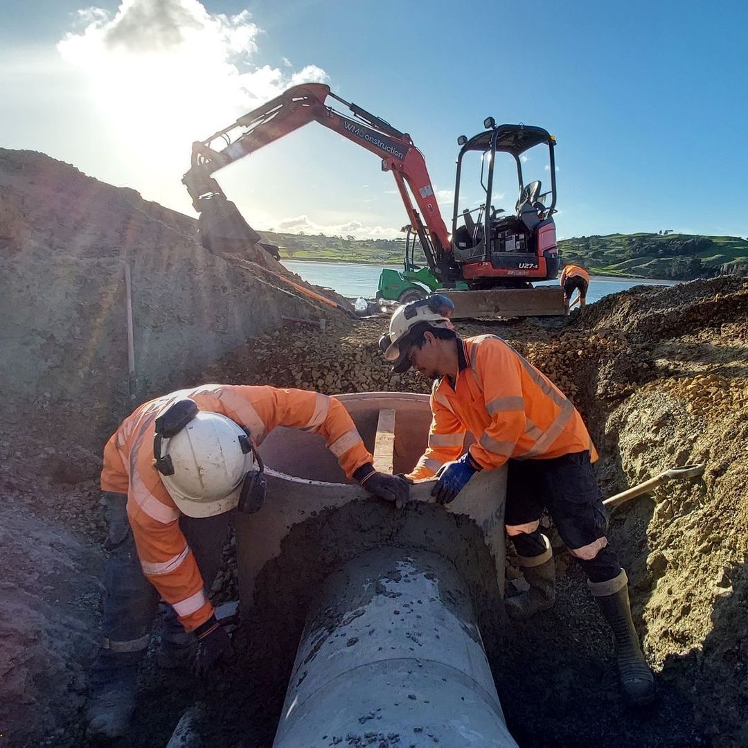 Two construction workers are working on a pipe in the dirt