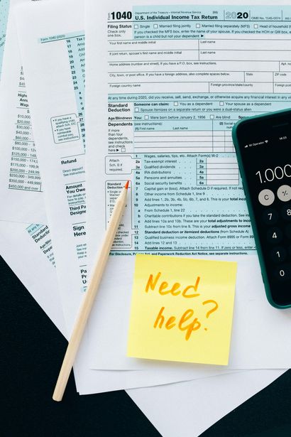 A calculator and a pencil are on a table next to a sticky note that says need help.