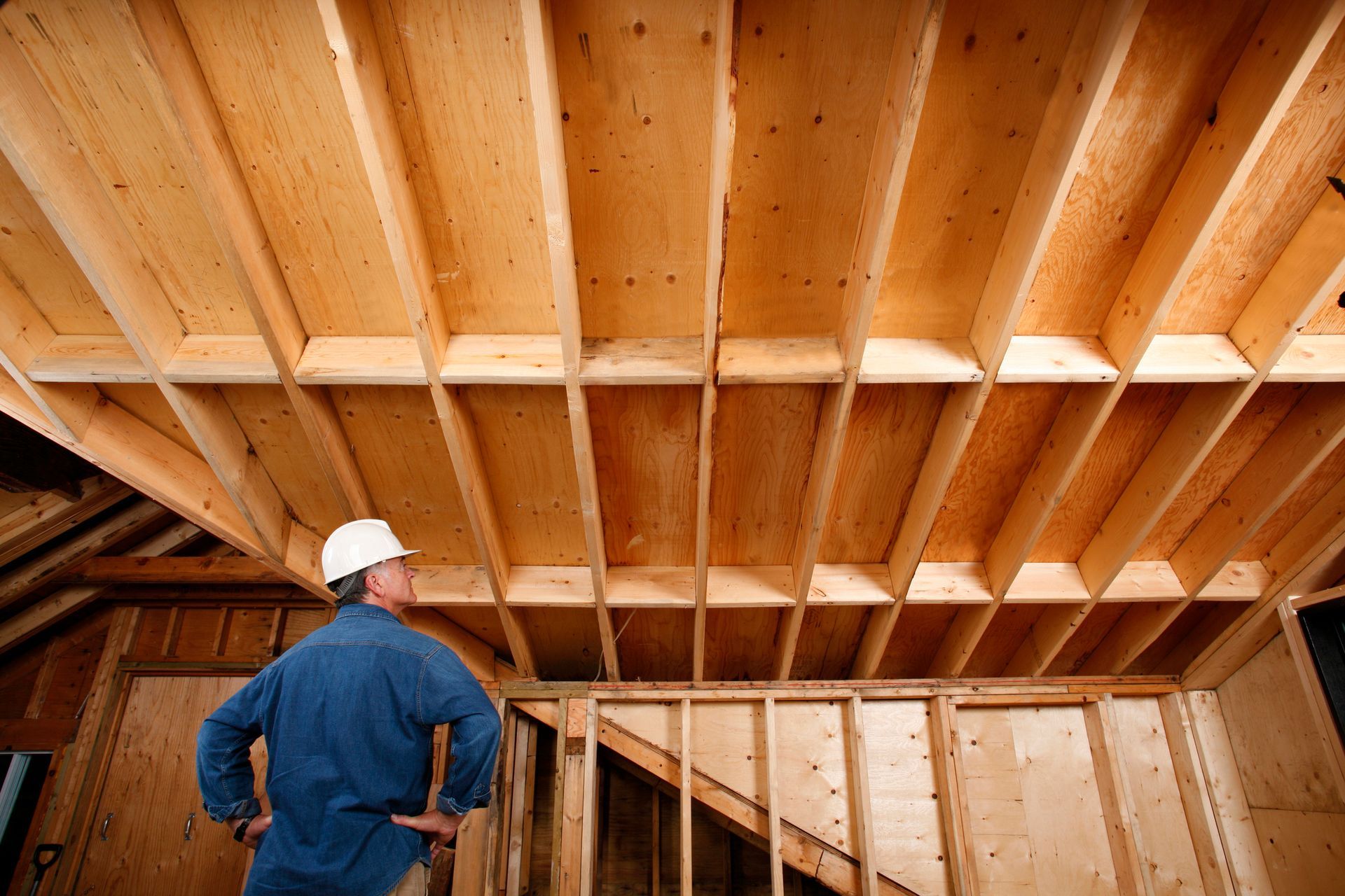 A man in a hard hat is looking up at the ceiling of a house under construction.