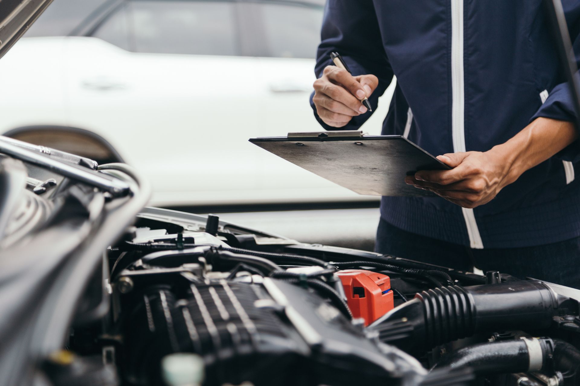 A person inspects a car engine with a clipboard and pen during a registration check.