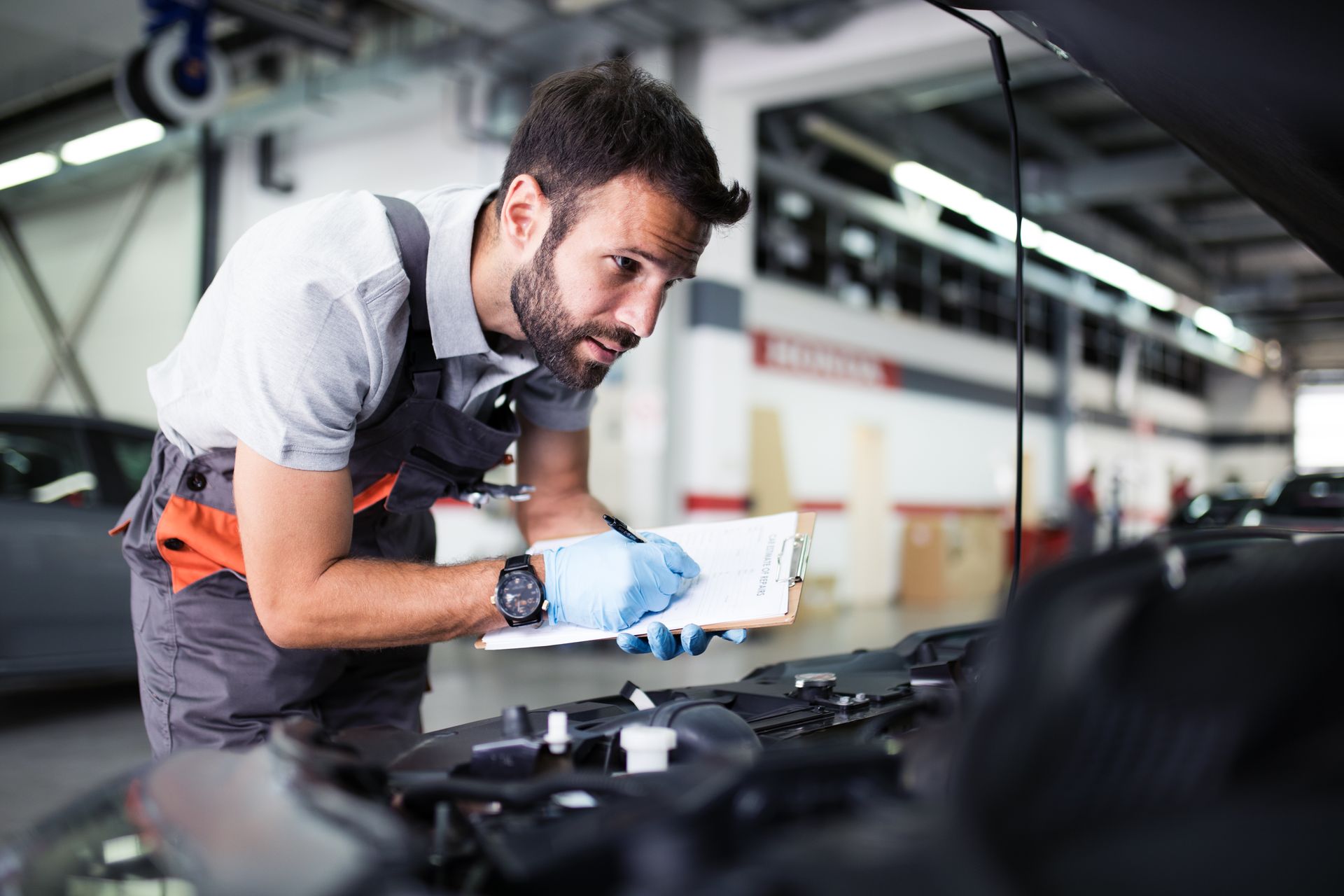 Mechanic checking a car engine and writing notes on a clipboard during logbook service.