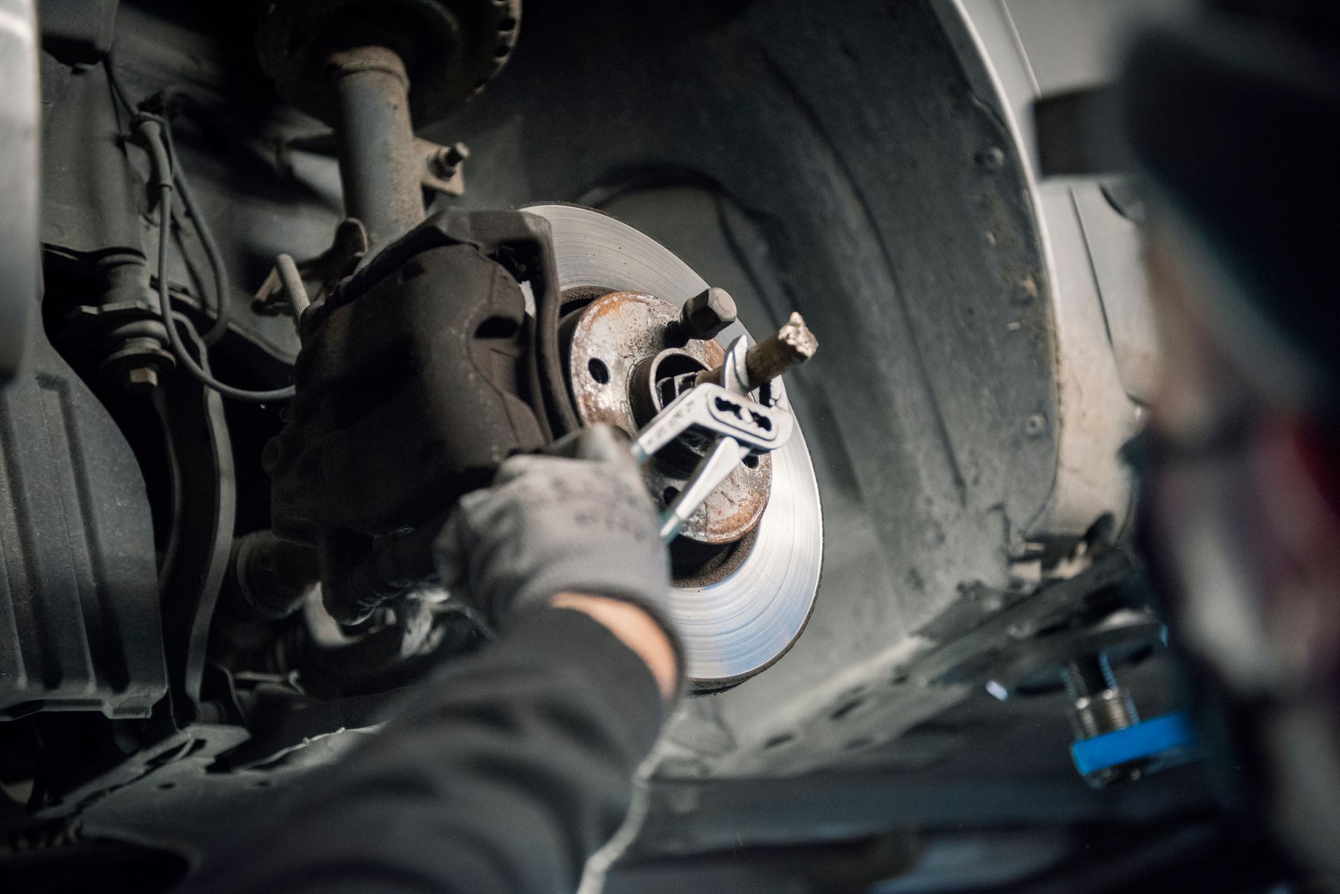 A mechanic using a tool to check a brake disc and calliper assembly on a vehicle wheel hub