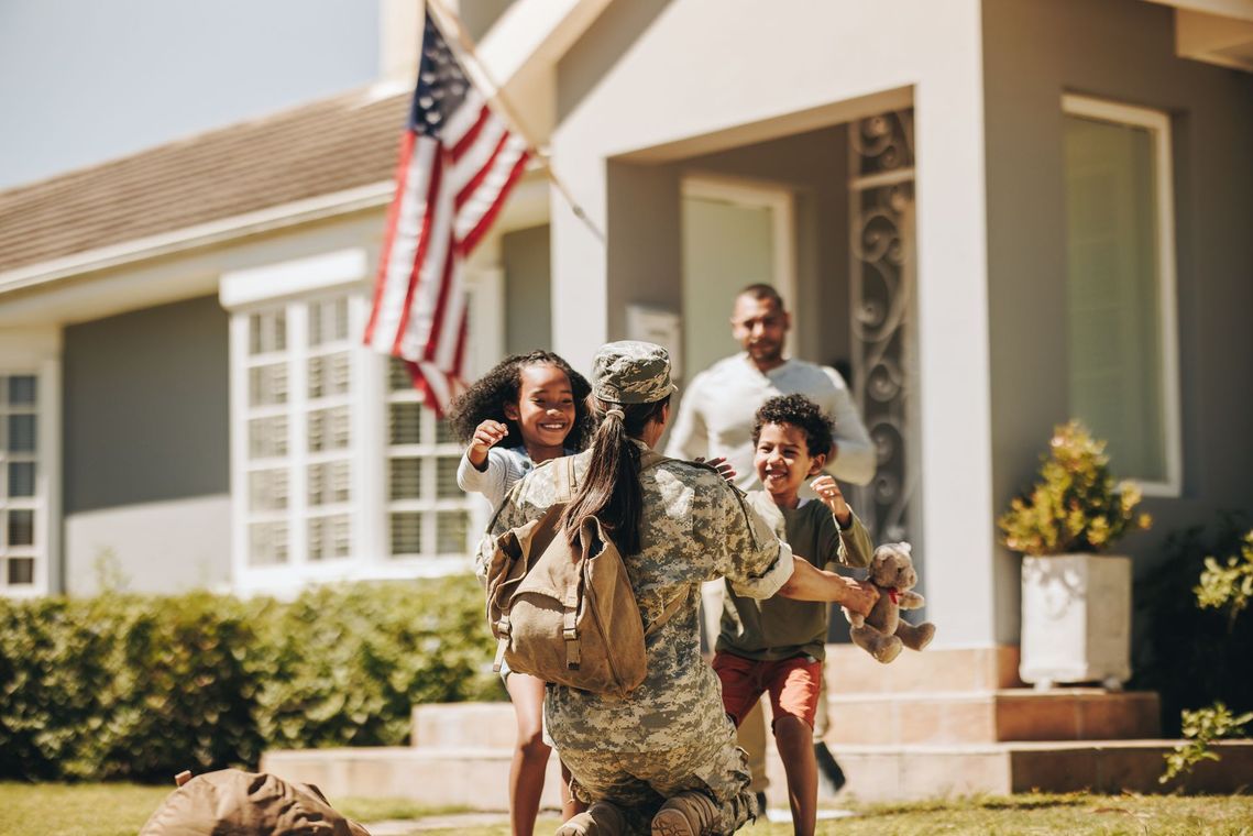 A soldier is kneeling down in front of a house with his family.