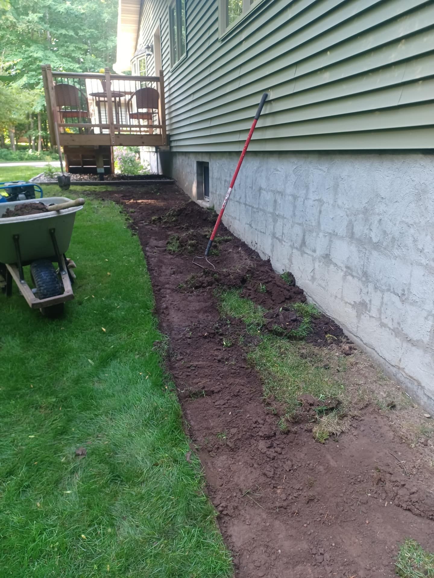 A wheelbarrow is sitting in the grass next to a house.