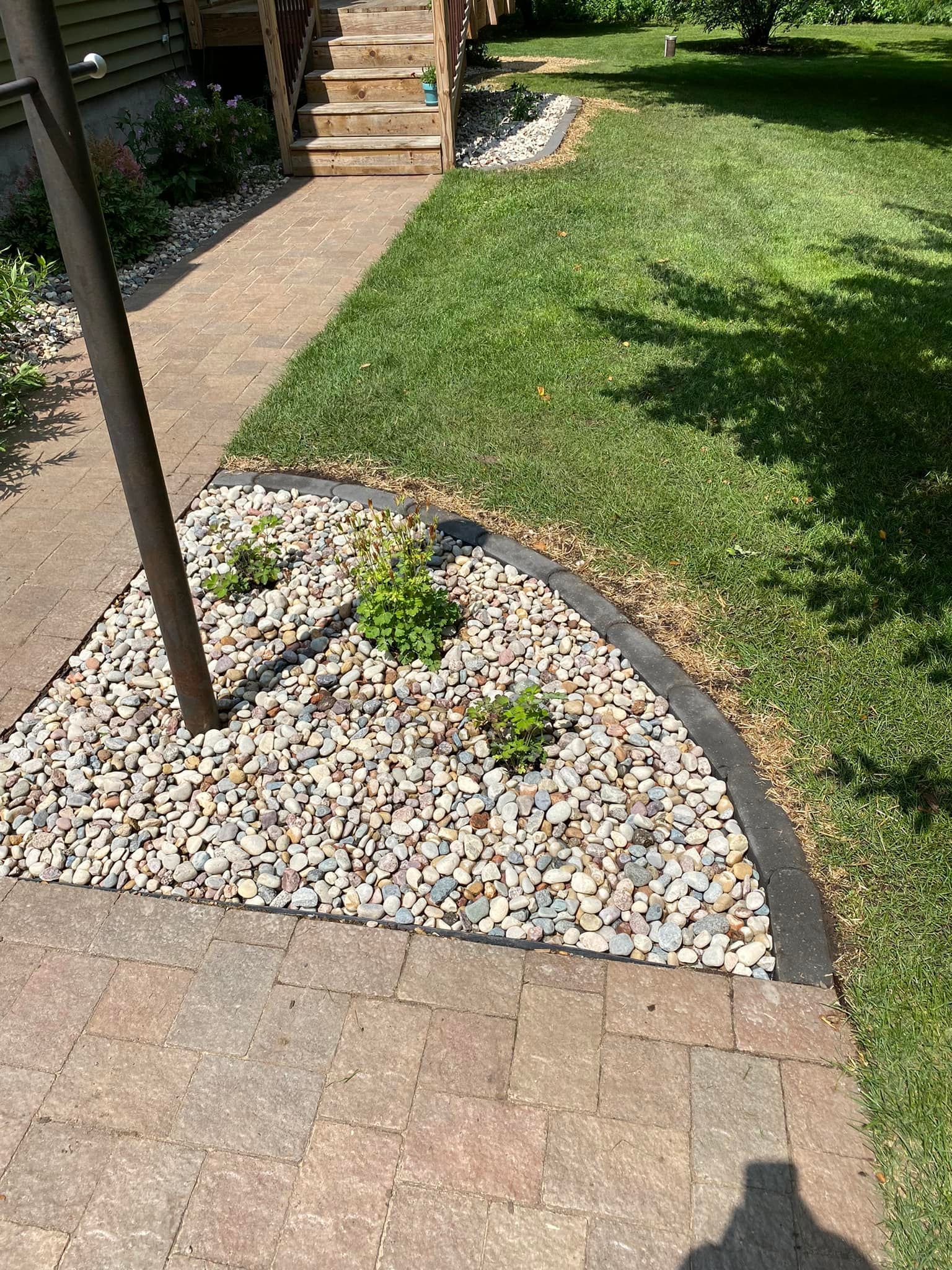 A brick walkway leading to a house with a gravel bed in the middle of the yard.